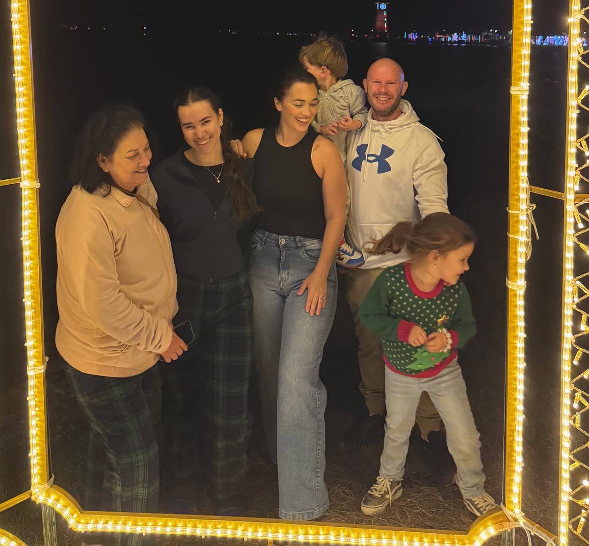Ana with three generations of her own family inside a lit Christmas arch at night, her youngest walking through the frame mid-step