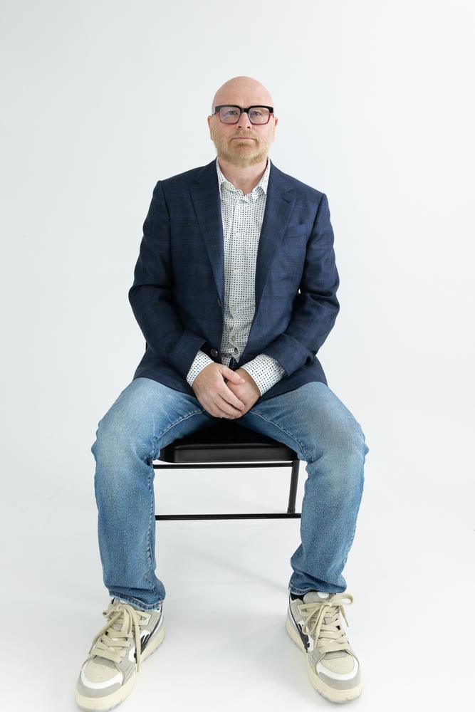 Relaxed full-length portrait of a man seated on a stool against white