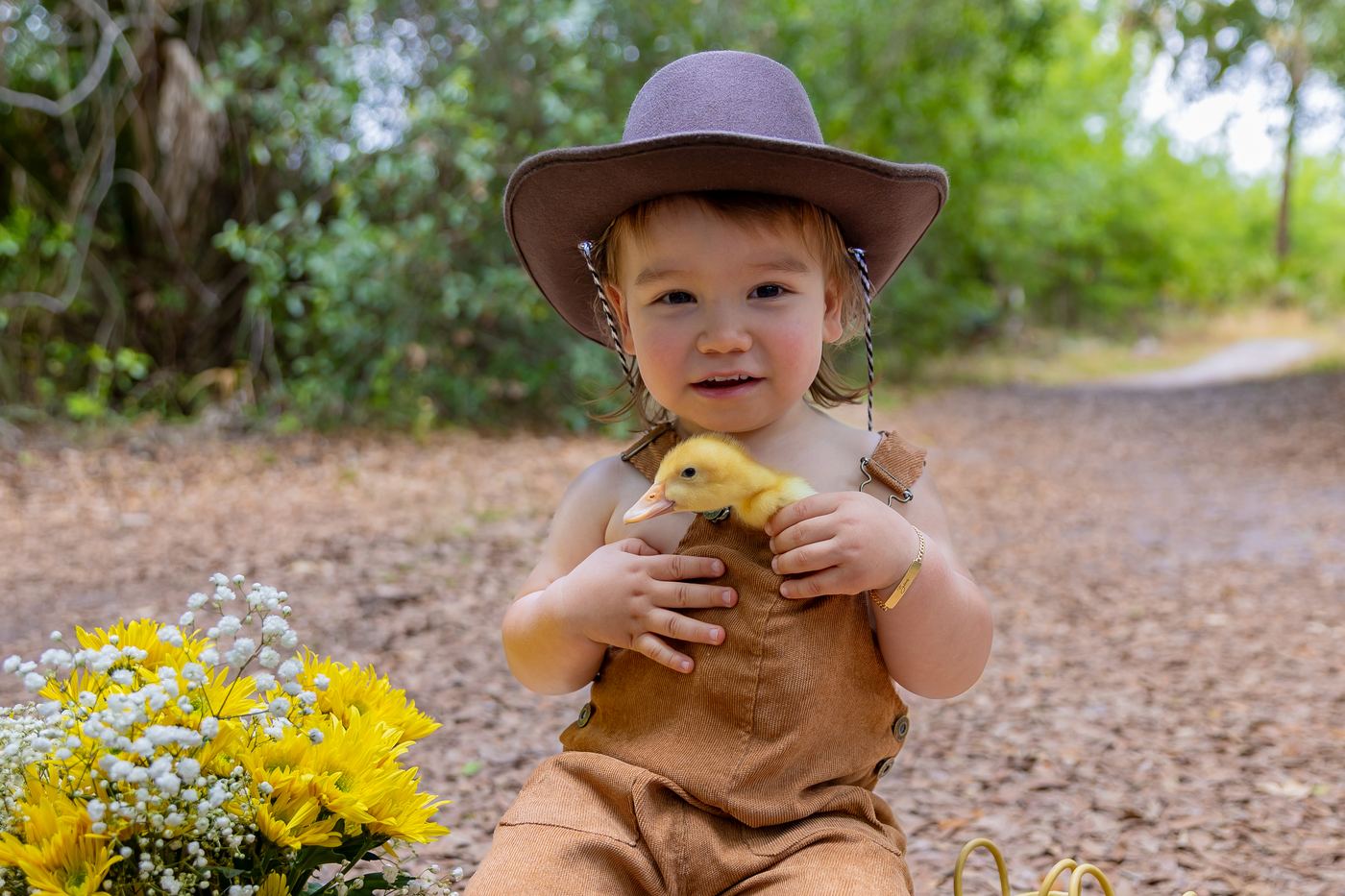 Little boy in overalls and a cowboy hat holding a duckling at a spring mini session in Southwest Florida