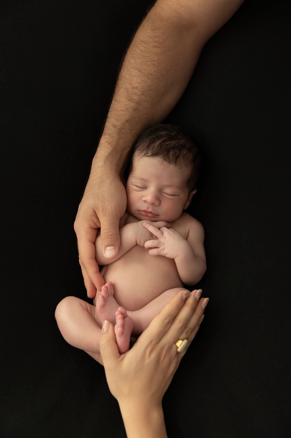Parents' hands gently cradling their sleeping newborn during an in-studio newborn session in Cape Coral