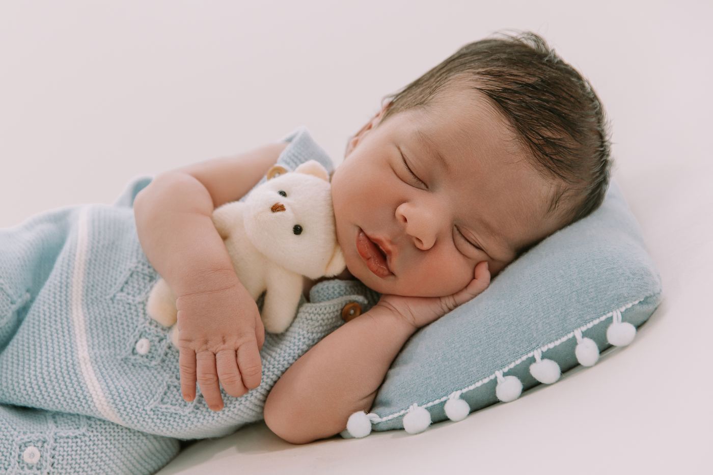 Newborn in a blue knit set snuggled with a teddy bear at the Cape Coral newborn studio
