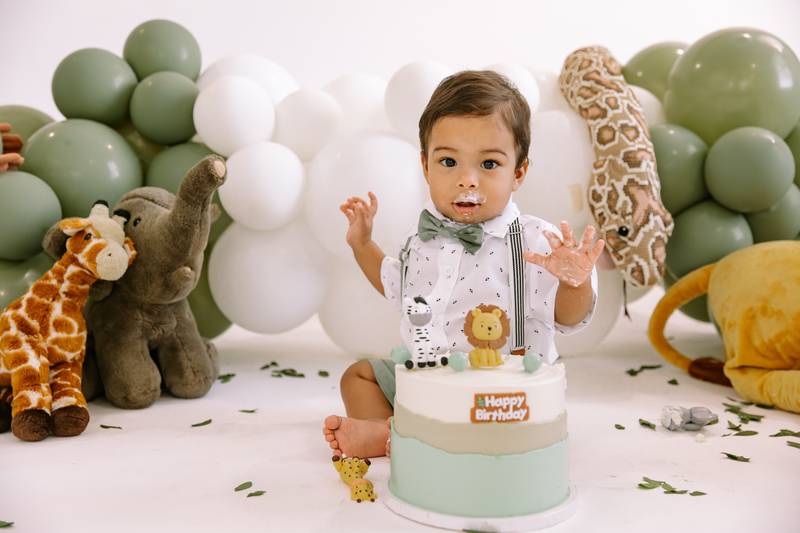 Baby boy digging into his cake at a safari-themed first birthday cake smash in the Cape Coral studio