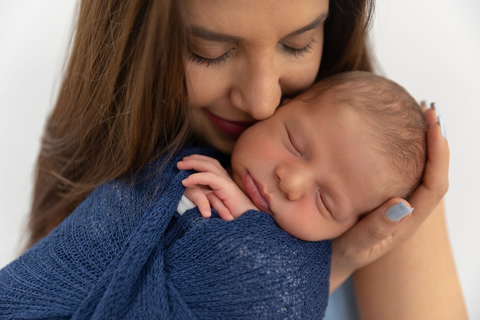 Mother in blue cradling her sleeping newborn in soft light — newborn session by Cape Coral photographer Ana Rousseau