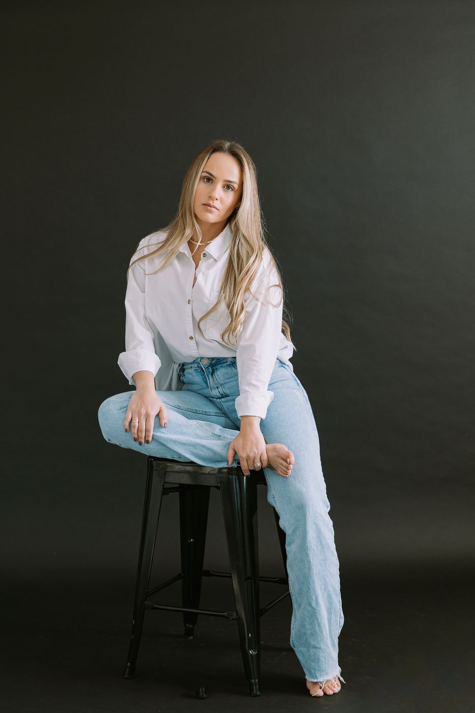 Relaxed personal branding portrait in a white shirt and jeans on a deep green backdrop