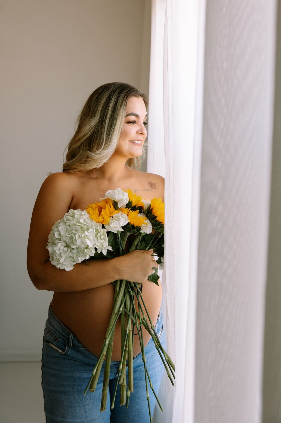 Expecting mother holding flowers in soft window light, maternity session at the Cape Coral studio