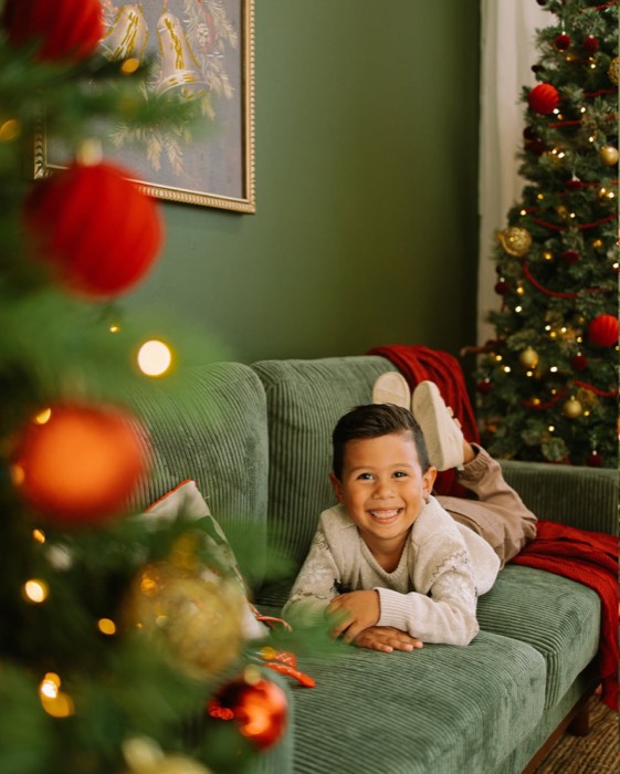 Boy laughing on the studio couch, framed through the branches of the Christmas tree