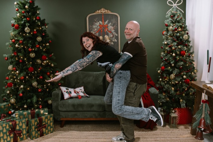 Couple laughing mid piggyback ride between two Christmas trees