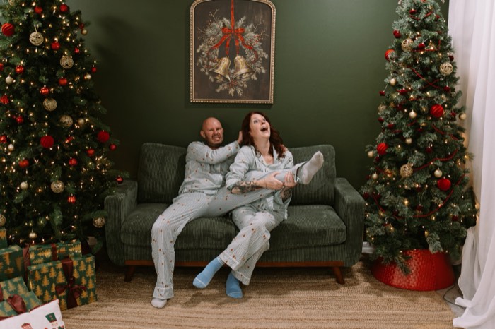 Couple in holiday pajamas cracking up on the studio couch